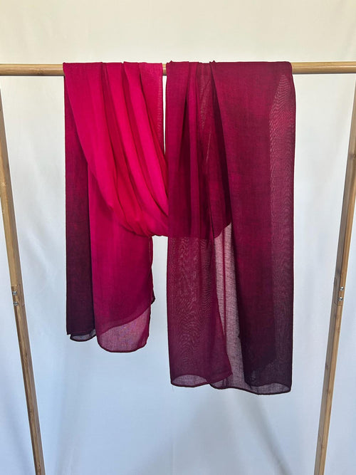 Lightweight magenta and burgundy scarves drape elegantly over a wooden garment rack against a white background.