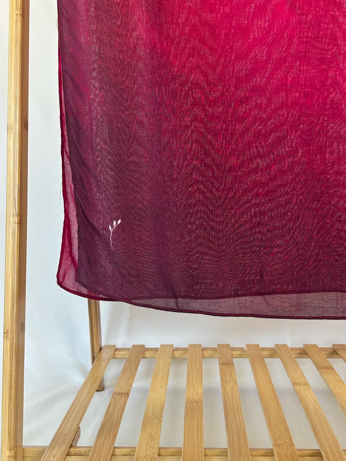A sheer maroon ombre scarf with a small white leaf embroidery hangs gracefully from a bamboo clothing rack.