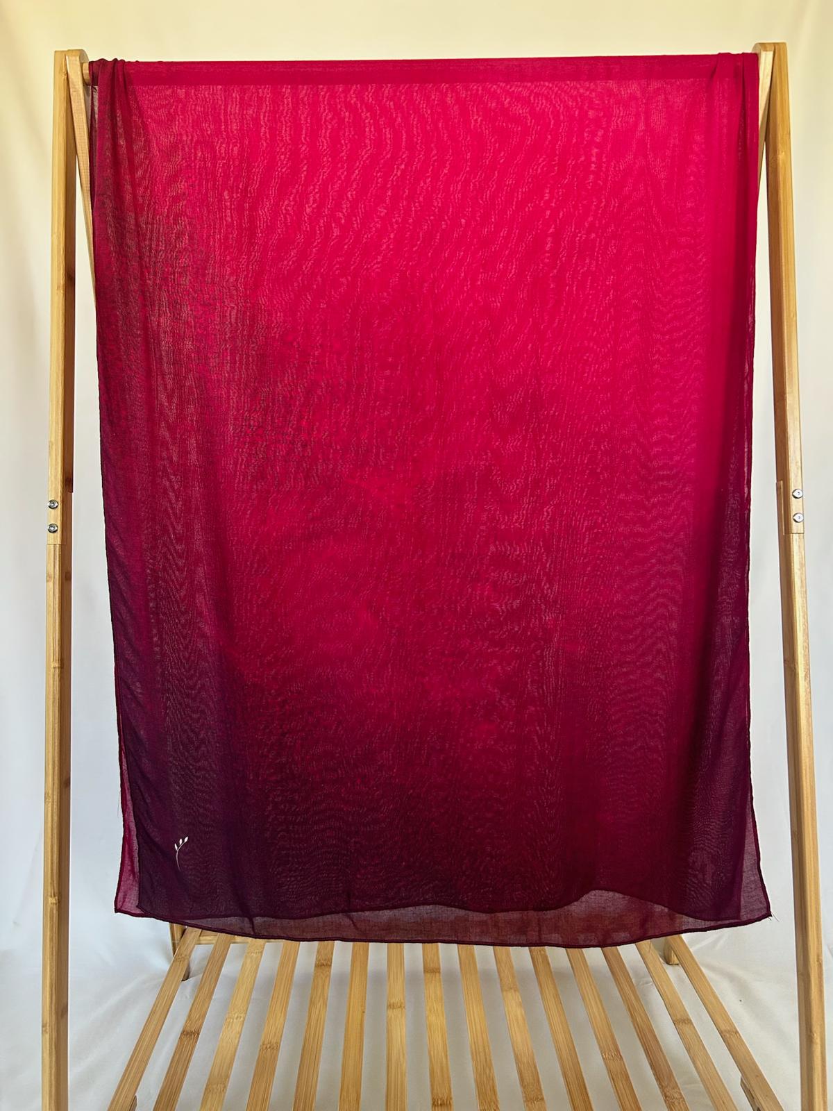 A lightweight magenta and purple ombre scarf hangs from a light wood rack, showcasing its delicate rippled texture and vibrant color gradient.