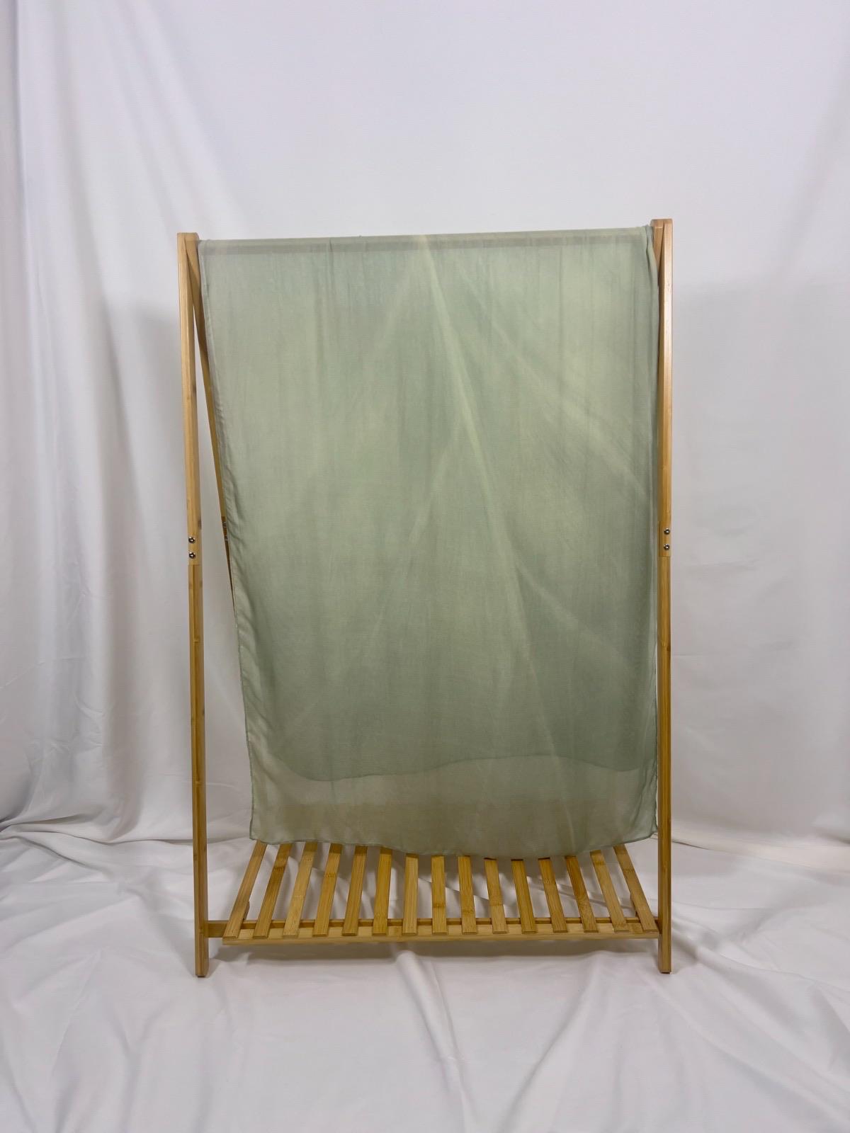 A light green sheer scarf drapes over a bamboo wooden garment rack with a slatted bottom shelf.