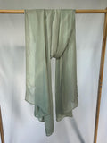 A lightweight sage green semi-sheer scarf with a small white embroidered leaf hangs from a bamboo clothing rack against a plain white background.