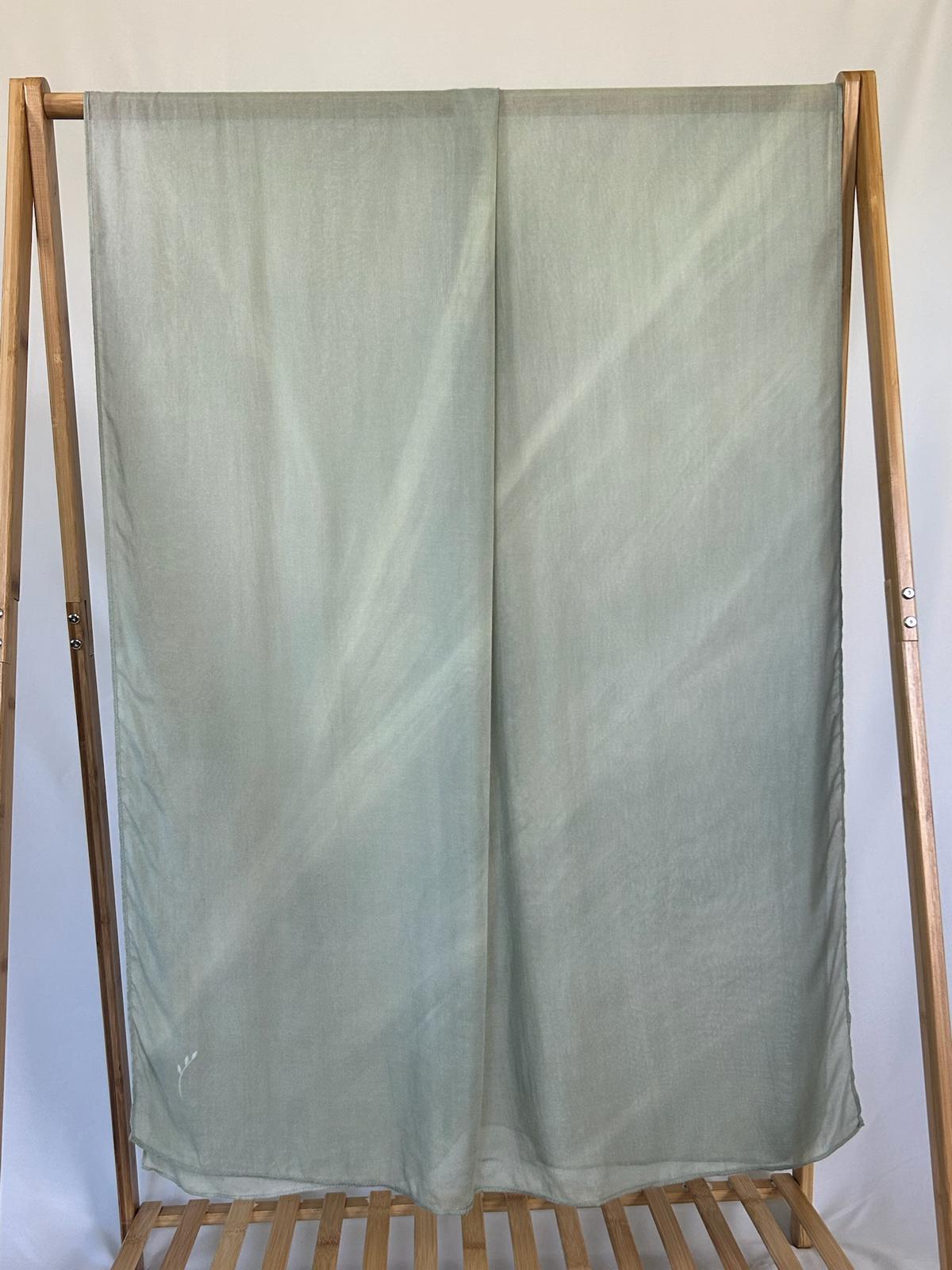A sheer sage green fabric with a delicate embroidered leaf drapes over a wooden clothing rack.