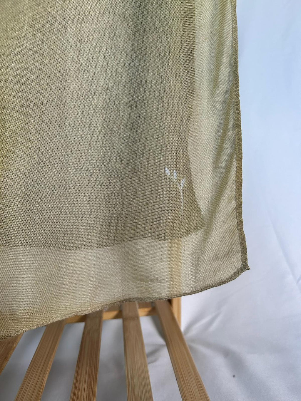 A lightweight olive green sheer scarf with a delicate white embroidered floral motif drapes over a wooden rack.