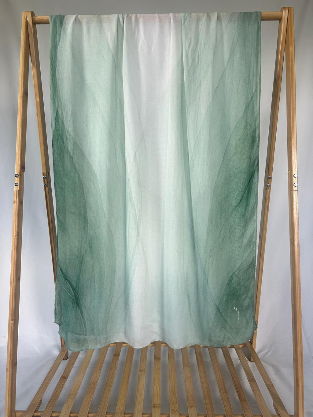 A lightweight green and white ombre scarf drapes elegantly over a wooden bamboo rack.
