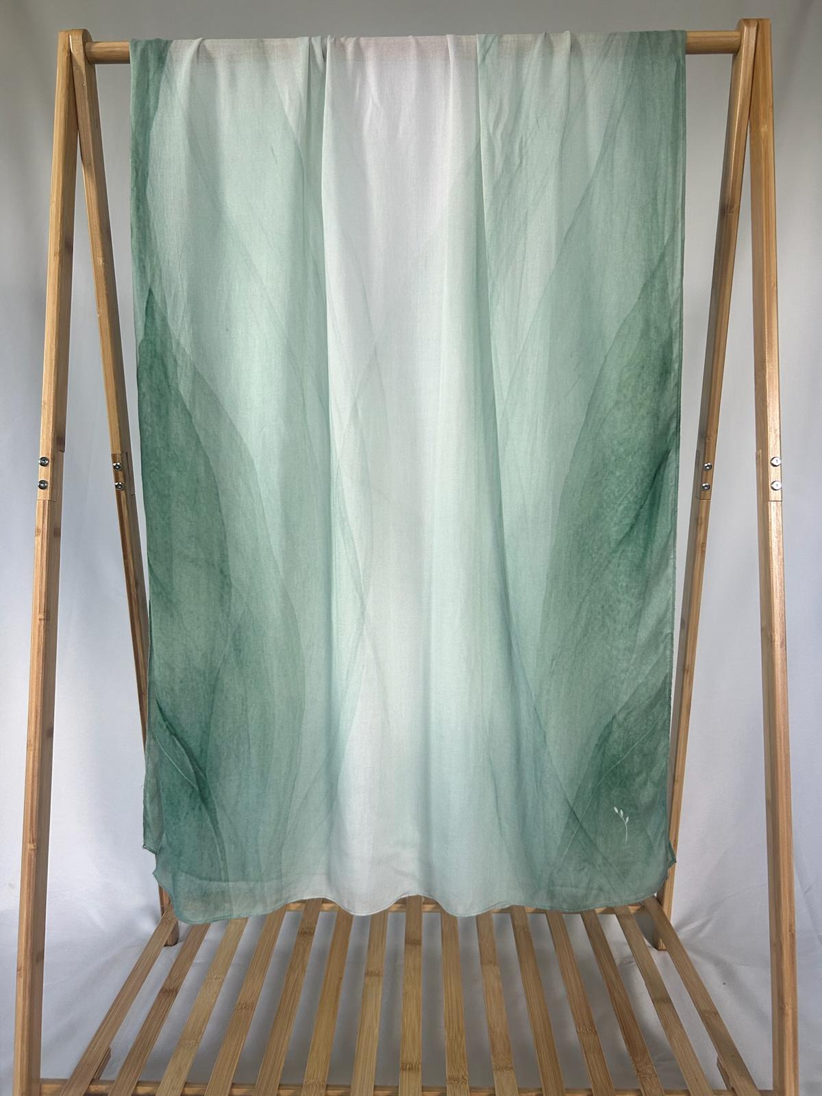 A lightweight green and white ombre scarf drapes elegantly over a wooden bamboo rack.