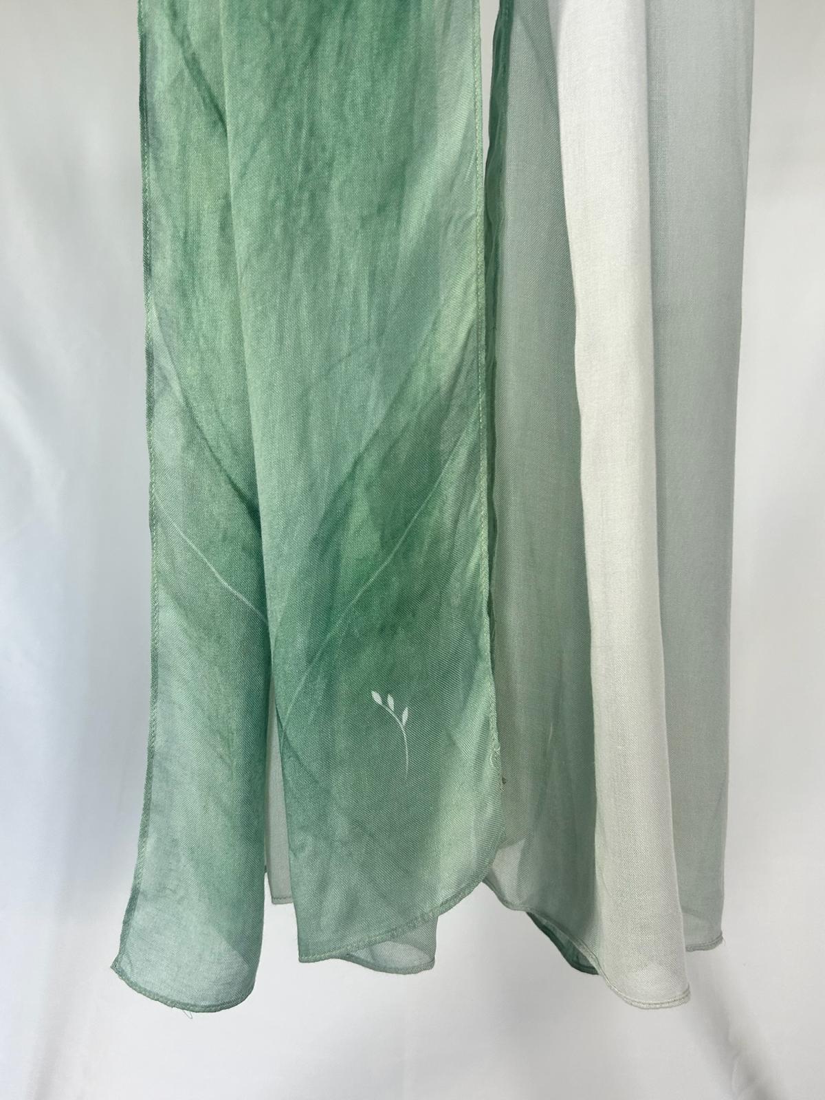 A sheer sage green and white scarf with a delicate white leaf print hangs in soft vertical folds against a neutral background.