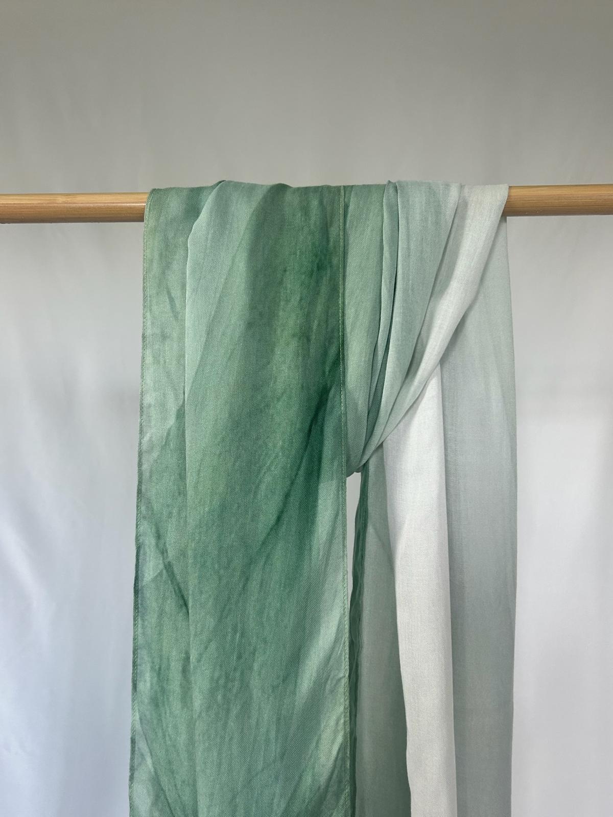 A lightweight green ombre silk scarf drapes elegantly over a wooden rod against a clean white background.