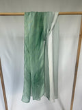A sheer green silk scarf with a subtle gradient pattern and a delicate leaf emblem hangs from a wooden display rack.