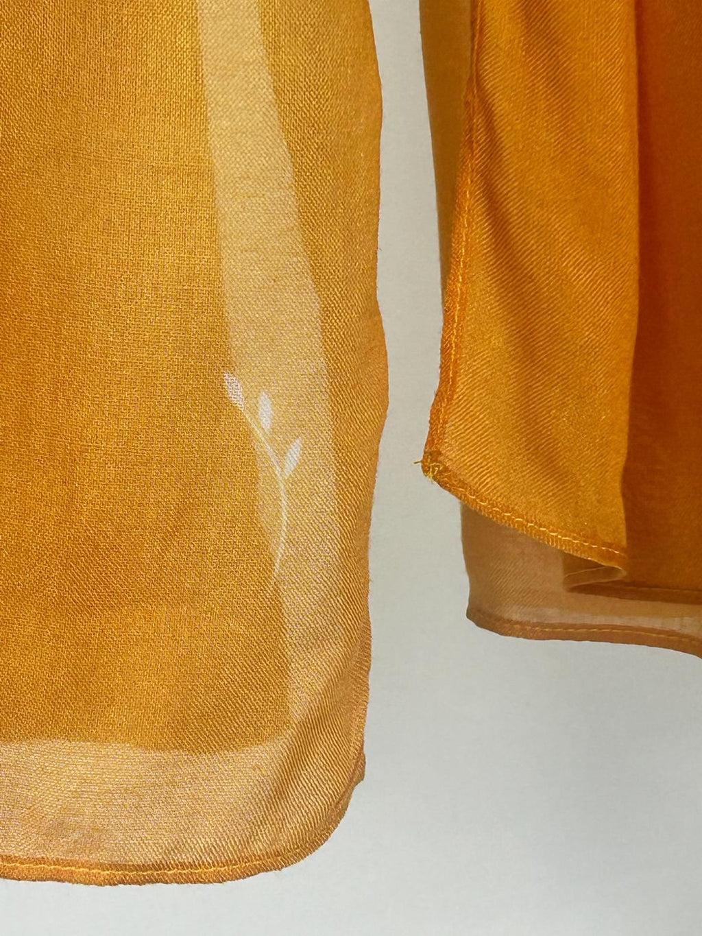 A close-up view showcases the fine weave and delicate white botanical print of a lightweight mustard yellow fabric.
