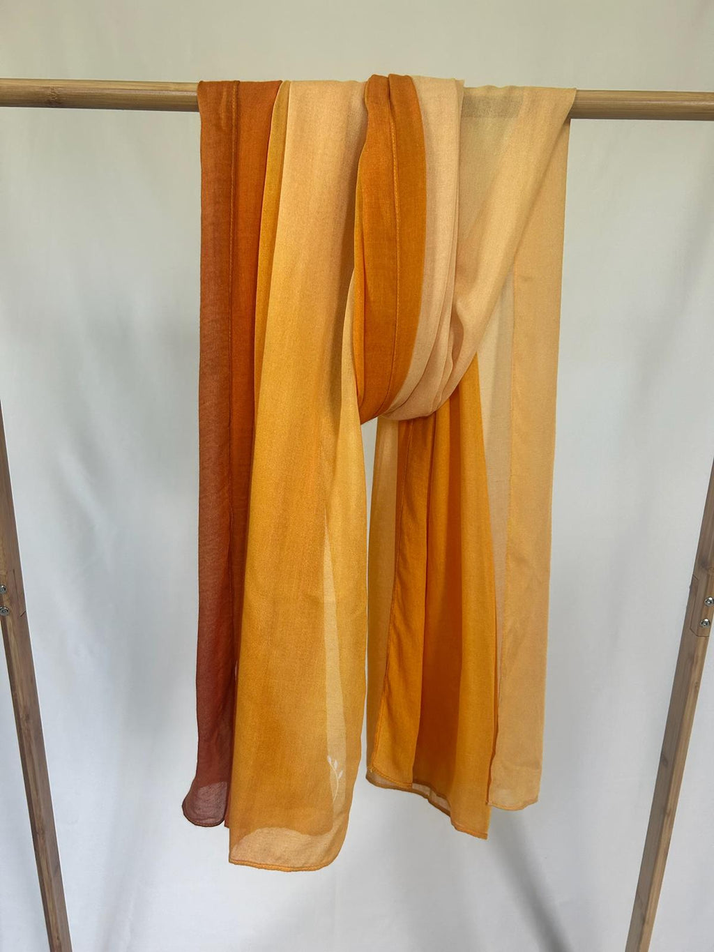 A lightweight ombre scarf in vibrant shades of orange and yellow drapes over a wooden clothing rack.