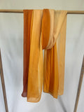 A lightweight ombre scarf in vibrant shades of orange and yellow drapes over a wooden clothing rack.