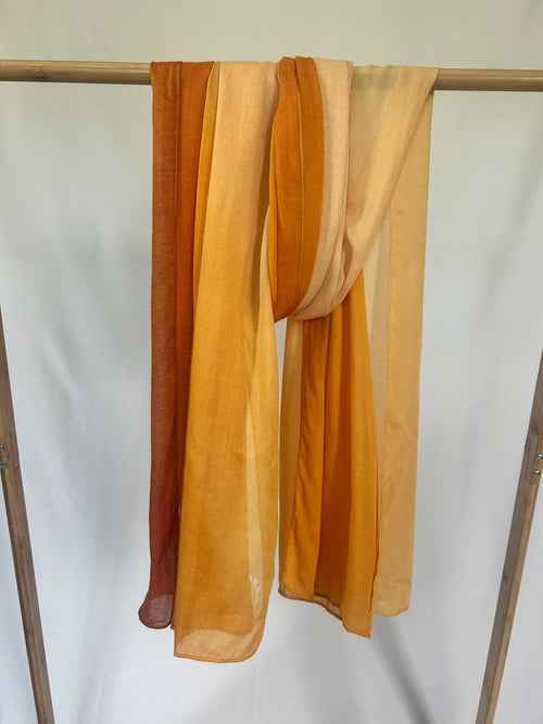 A lightweight ombre scarf in vibrant shades of orange and yellow drapes over a wooden clothing rack.