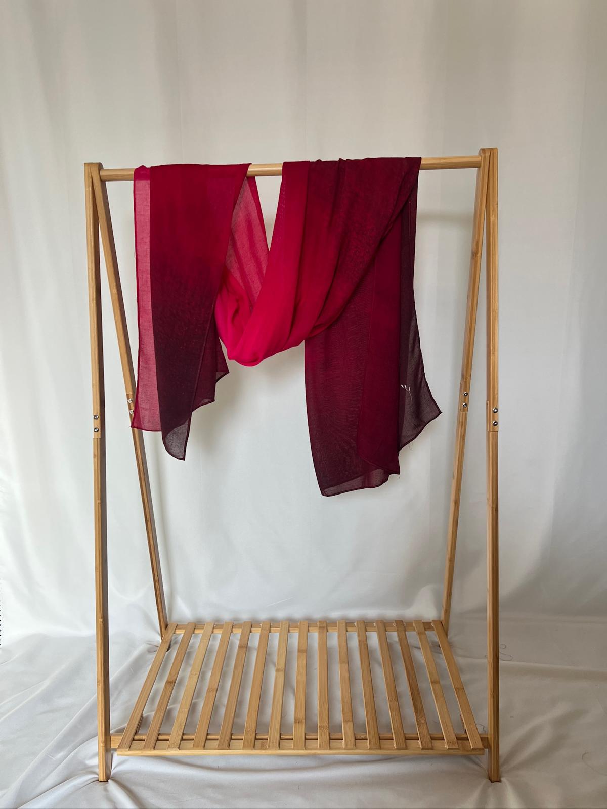 A vibrant red and burgundy ombre scarf drapes elegantly over a minimalist wooden clothing rack.