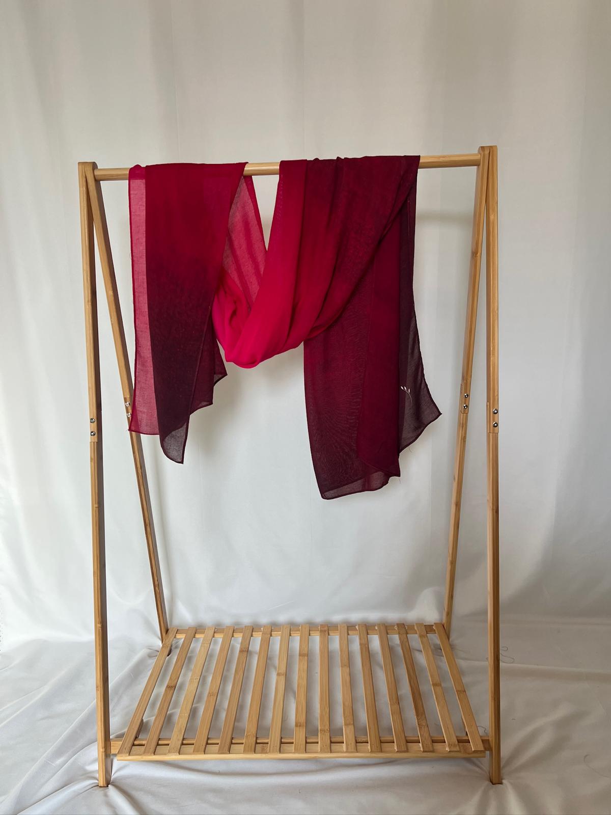 A vibrant red and burgundy ombre lightweight scarf drapes elegantly over a minimalist wooden clothing rack.